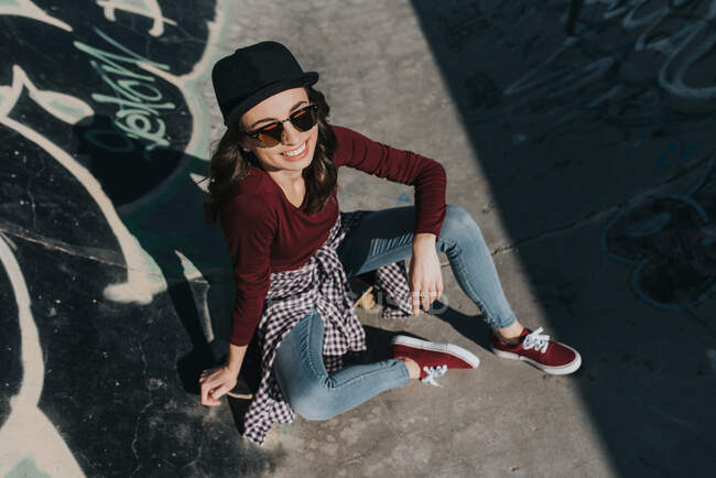 De dessus plan de jeune femme élégante dans skatepark souriant large dans la lumière du soleil. — Photo de stock