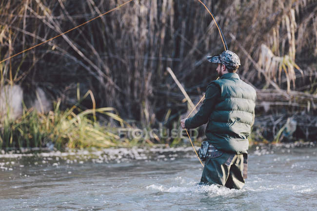 Rückansicht eines Mannes, der im Fluss steht und mit der Rute fischt — Stockfoto