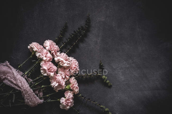 Плоский вид на кучу розовых гвоздик, связанных кружевами на каменной поверхности — стоковое фото