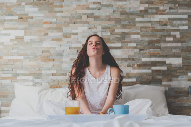 Девушка сидит перед подносом с завтраком на кровати — стоковое фото