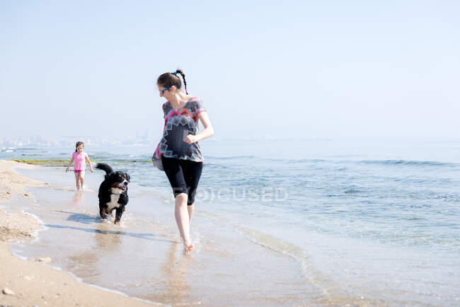 Happy family playing with dog on beach — Stock Photo