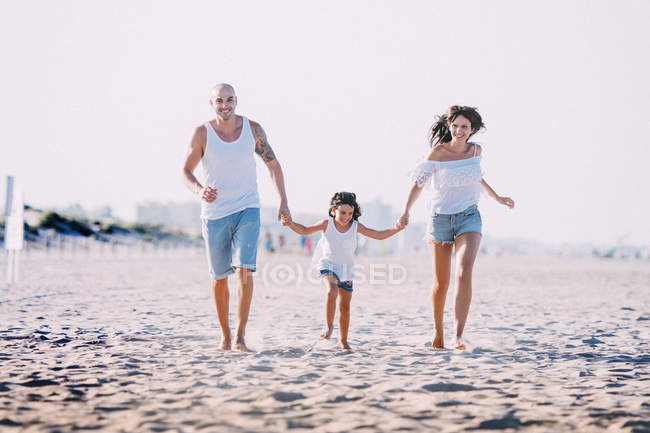 Портрет сім'ї, що біжить на пляжі і тримається за руки . — стокове фото