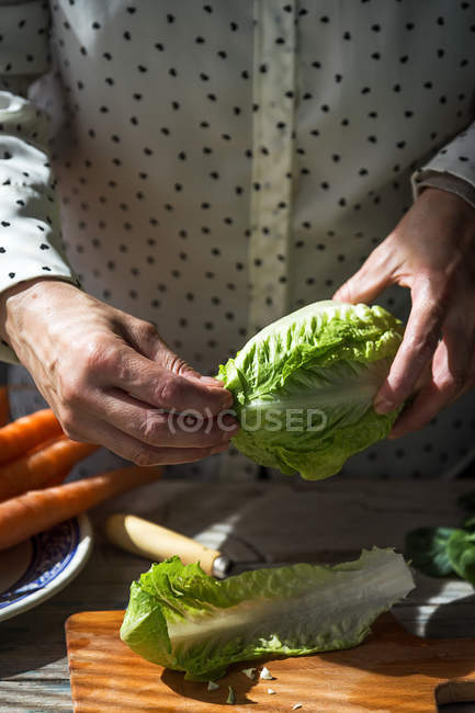 Vue rapprochée des mains féminines déchirant les feuilles de chou napa sur une planche de bois sur la table — Photo de stock