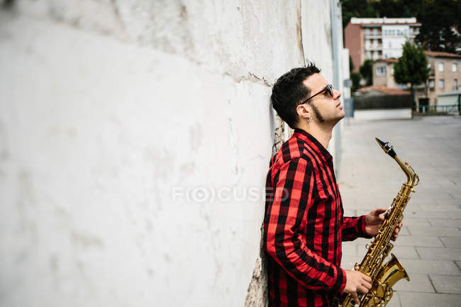 Джазовий музикант, спираючись на стіні і проведення саксофон — стокове фото