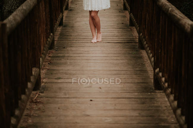 Низька частина дівчини в білій сукні позує на дерев'яному мосту — стокове фото