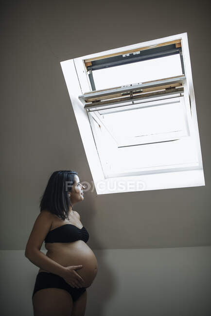 Embarazada mirando hacia arriba a la ventana abierta del desván. Vista lateral. - foto de stock