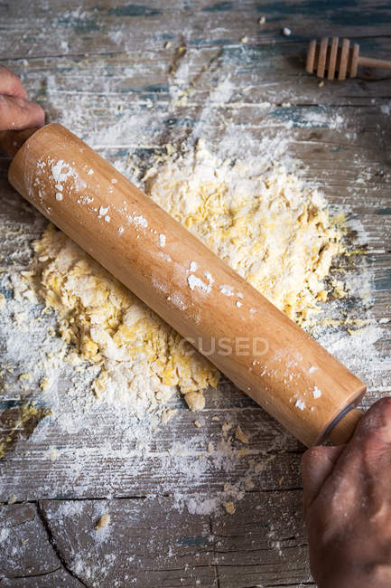Vue ci-dessus de la pâte à rouler mains avec rouleau à pâtisserie sur table rurale en bois — Photo de stock