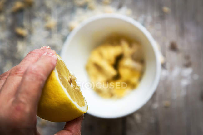 Above view of hand squeezing lemon in ceramic bowl with dough — Stock Photo