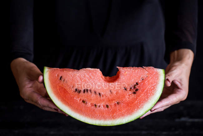 Close-up de mulher segurando cunha fresca de melancia no fundo escuro — Fotografia de Stock