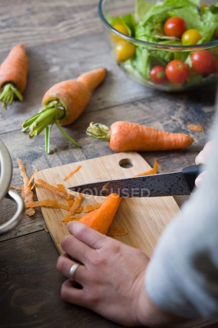 Coltivazione mani taglio carota su tavola di legno — Foto stock