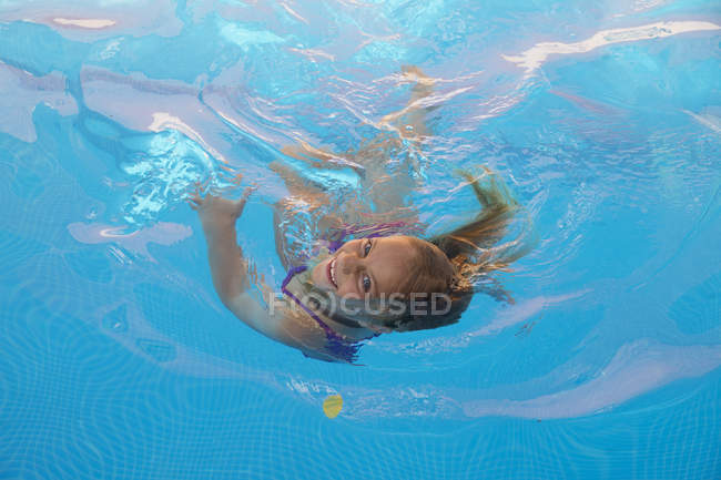 Bambino che nuota in piscina con acqua turchese e guarda la macchina fotografica — Foto stock