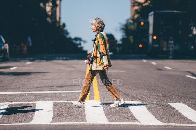 Vista lateral de anciana elegante mujer asiática cruzando la calle en la ciudad. - foto de stock