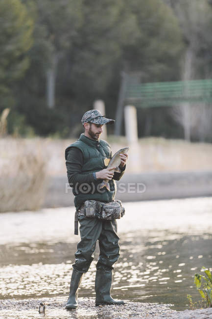 Pescador posando con la captura en la orilla del río - foto de stock