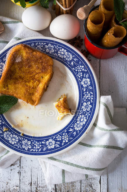 Top view of ornate ceramic plate with sweet toasts and mint on towel over table with ingredients and sweet tubes — Stock Photo
