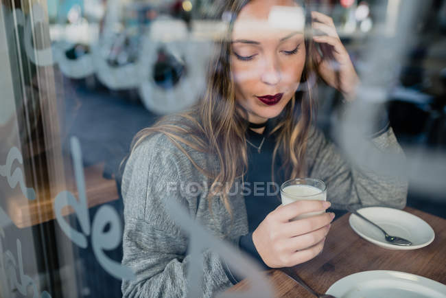 Menina bebendo leite atrás de vidro de beanery . — Fotografia de Stock