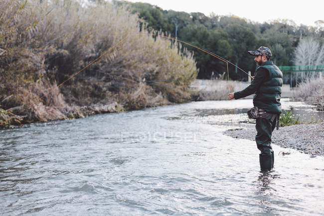 Side view of man standing in shallow river and fishing with rod — Stock Photo