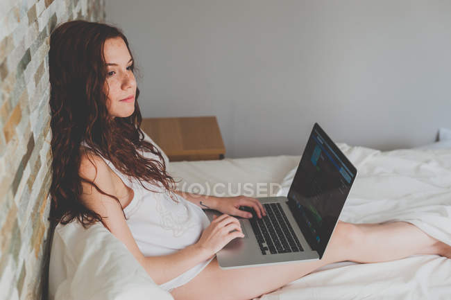 Женщина отдыхает в постели и с помощью ноутбука — стоковое фото