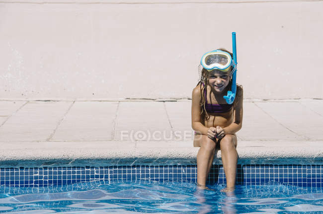 Enfant en masque de plongée assis au bord de la piscine et regardant la caméra — Photo de stock