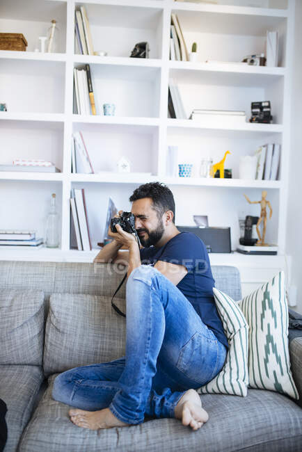 Photographer taking camera shot, while sitting on sofa. — Stock Photo
