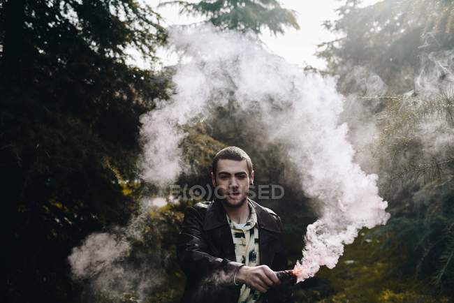 Портрет стильного чоловіка махає рукою з димом свічки серед лісу і дивиться на камеру — стокове фото