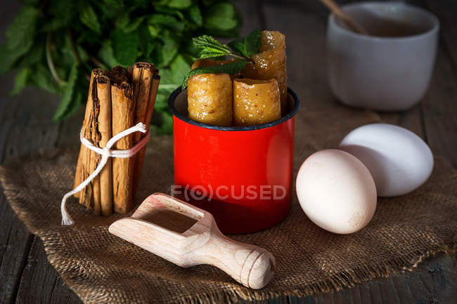Bodegón de taza roja con dulces e ingredientes en el saqueo - foto de stock