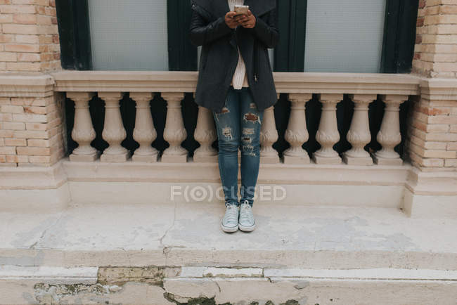 Обрезанное изображение женщины, опирающейся на парапет и использующей смартфон — стоковое фото