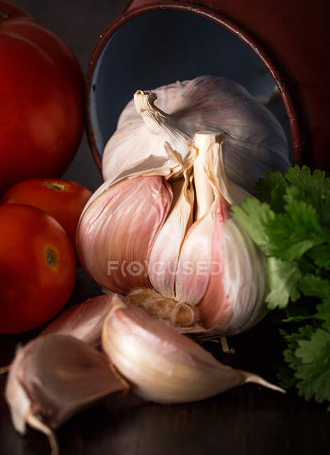 Close-up of fresh garlic cloves with tomatoes and parsley — Stock Photo