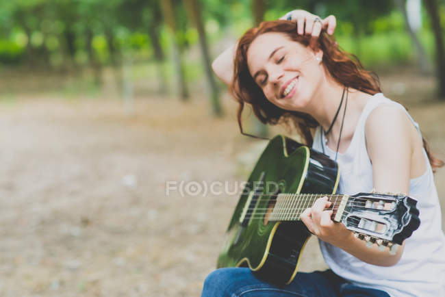 Portrait de fille ridée souriante ajustant les cheveux et prête à commencer à jouer de la guitare à la campagne wods — Photo de stock