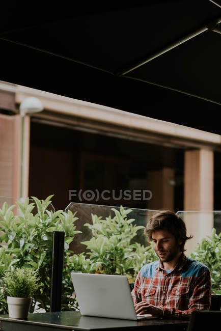 Portrait of bearded man sitting at cafe terrace table and using laptop — Stock Photo