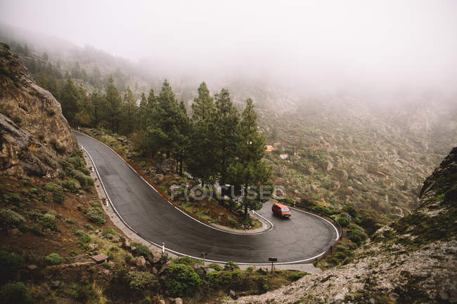 Car driving on winding road in mountains on foggy day — Stock Photo