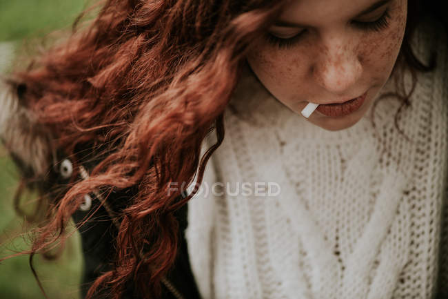 Портрет рыжей девушки с сигаретным фильтром во рту, смотрящей вниз — стоковое фото