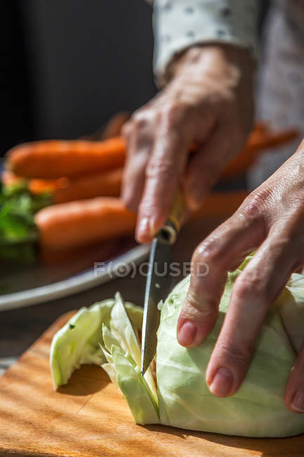 Vue rapprochée des mains féminines tranchant le chou avec un couteau sur une planche de bois — Photo de stock