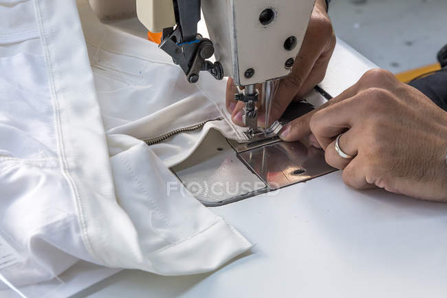 Manos de los cultivos de costura en la maquinaria de tela blanca - foto de stock