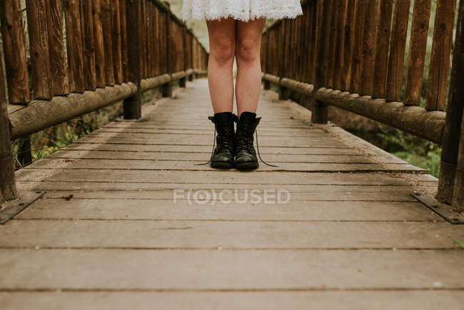 Section basse de fille en robe blanche debout sur un pont en bois — Photo de stock