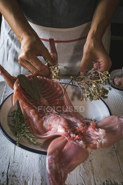 Primer plano de la mujer que sostiene la canal de conejo crudo con ingredientes en la mesa de madera - foto de stock