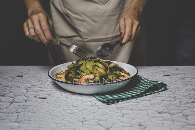 Мидсекция женщины, держащей вилку и ложку над итальянской зеленой тальятеллой с морепродуктами — стоковое фото