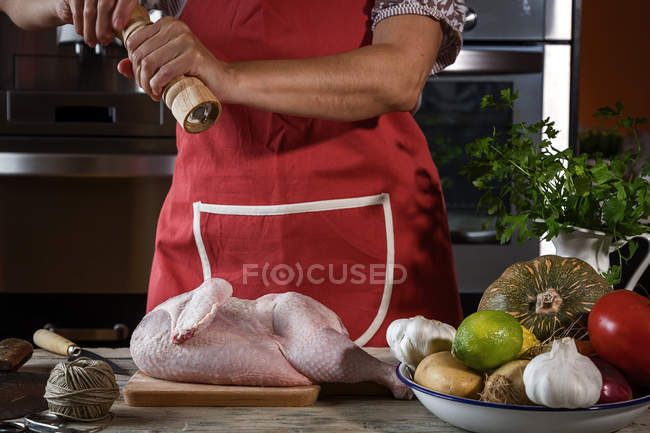 Close-up de mulher polvilhando frango cru com pimenta — Fotografia de Stock