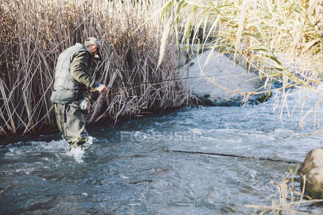 Vista lateral do homem de pé no rio e pesca com vara no campo de outono — Fotografia de Stock