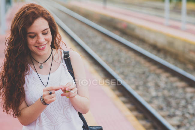 Portrait of girl with freckles and windy red hair lighting cigarette at railway platform — Stock Photo