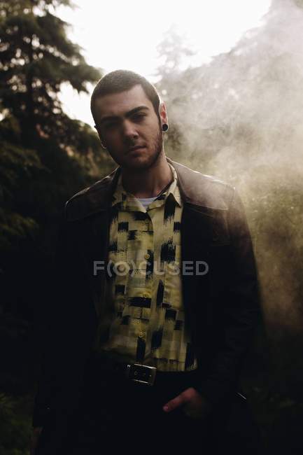Porträt eines Mannes, der in farbigem Rauch zwischen Wäldern steht und in die Kamera blickt — Stockfoto