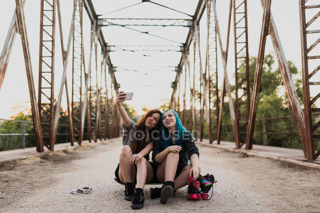 Две девочки сидят на скейтборде и делают селфи . — стоковое фото