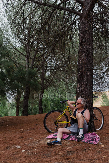 Портрет літнього чоловіка, який дивиться з книгою в руці на дереві з велосипедним парком позаду — стокове фото