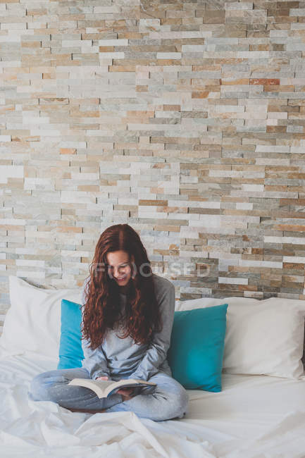 Girl sitting on bed and reading book — Stock Photo