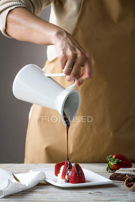 Sección media de la hembra verter la cobertura de chocolate en el postre de fresas en el plato con frasco - foto de stock