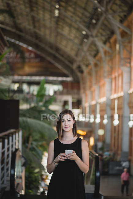 Portrait of young girl using smartphone near escalator and looking camera — Stock Photo