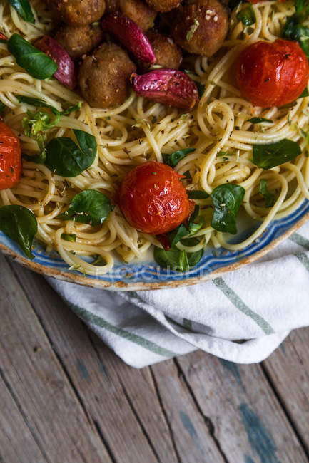 Crop image of plate of pasta with basil and cherry tomatoes on towel over rustic wooden table — Stock Photo