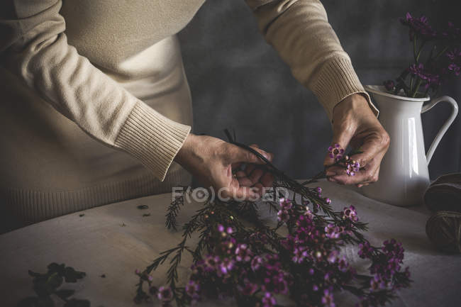 Partie médiane du fleuriste femelle coupant fleur rose avec ciseaux sur la table avec vase — Photo de stock