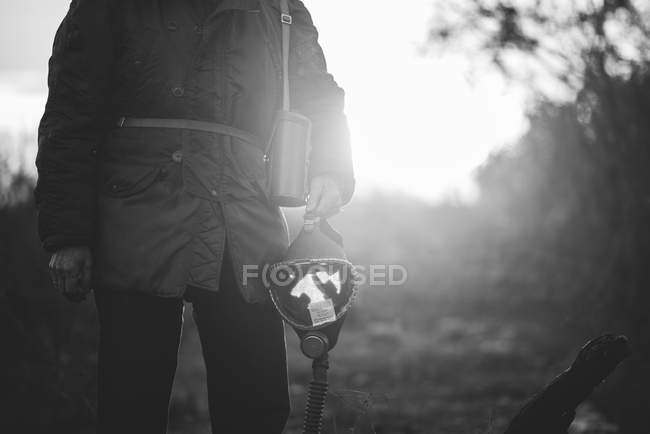 Низька частина людини, що стоїть на полі і тримає газову маску в руці — стокове фото