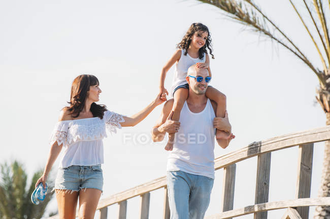 Веселый отец заботится о дочери на плечах во время прогулки с женой — стоковое фото