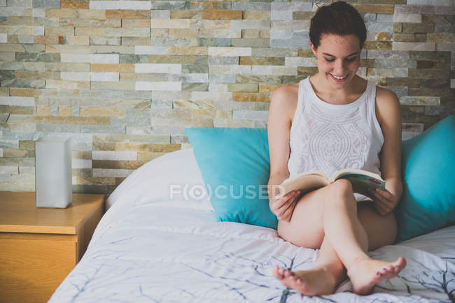 Chica sentada en la cama y leyendo libro - foto de stock